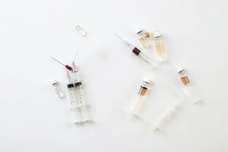 Kit de seringas e frascos de produtos estéticos dispostos sobre uma superfície branca, em plano detalhe, com luz de laboratório vinda de cima, em um momento estático.