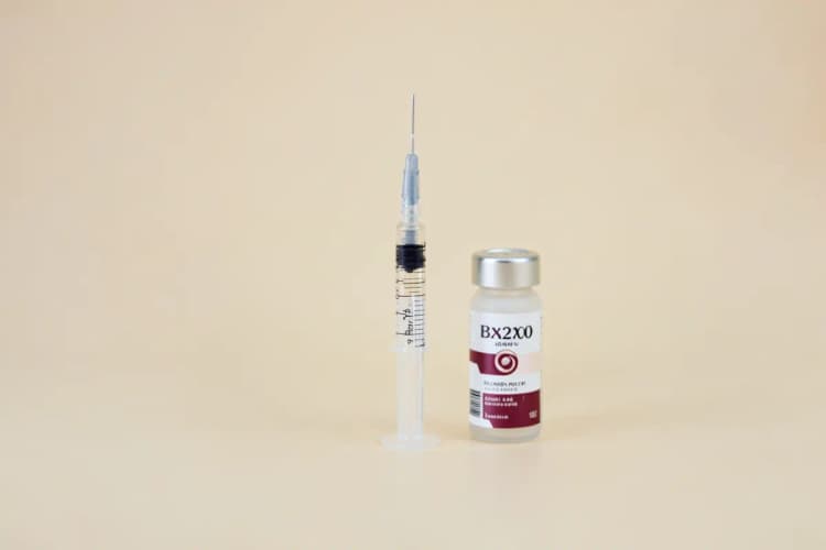 Seringa com líquido transparente ao lado de um frasco de botox, em close-up, com luz de clínica vinda da lateral, em um momento estático.